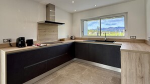 A modern kitchen with a large island, dark cabinetry, and a view of a vineyard through a large window. - IBARNIA - SUHESCUN - Gîte (SUHESCUN)