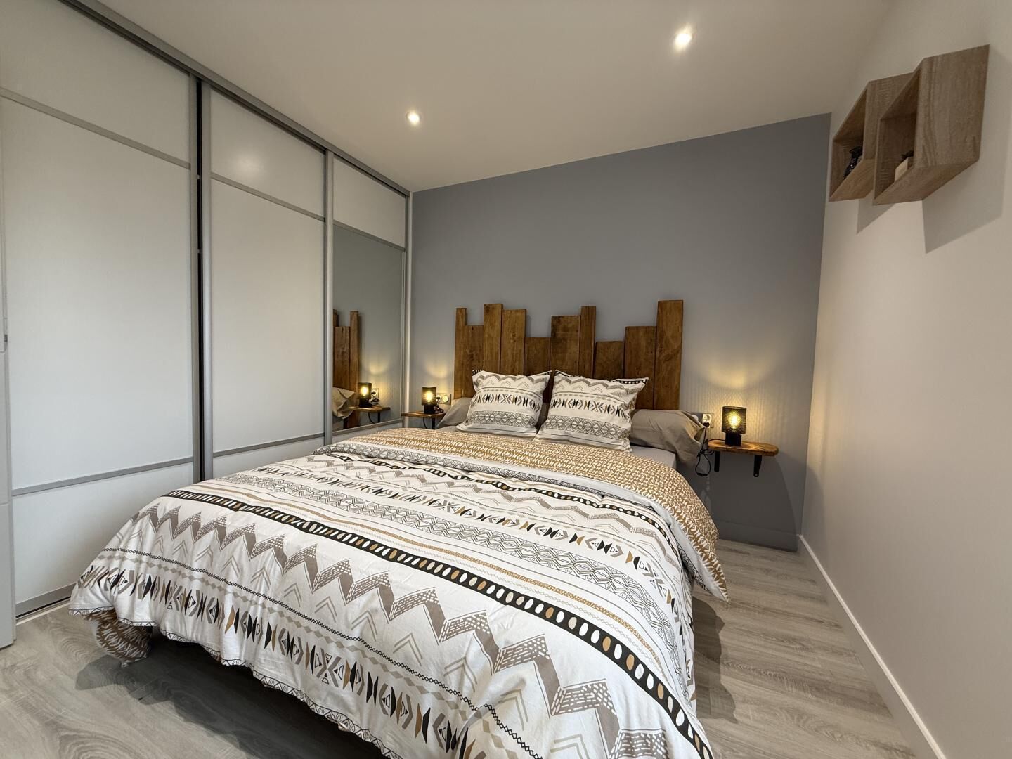 A modern bedroom with a large bed, wooden headboard, bedside lamps, and a sliding door.