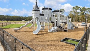 Un parc infantil amb una construcció semblant a un castell, tobogans i una zona tancada per una tanca.