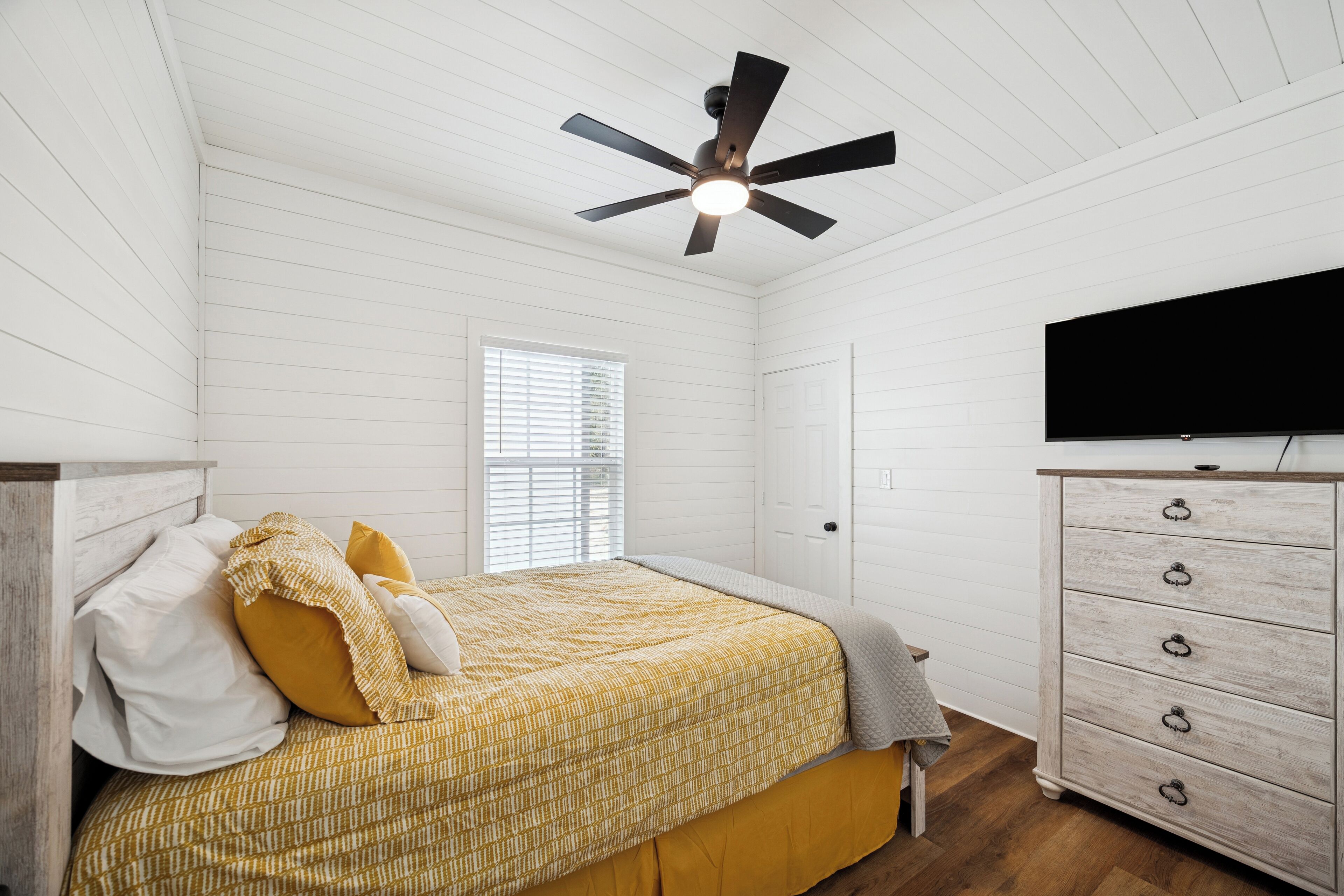 Un dormitorio con cama, cómoda, ventilador de techo y televisor.