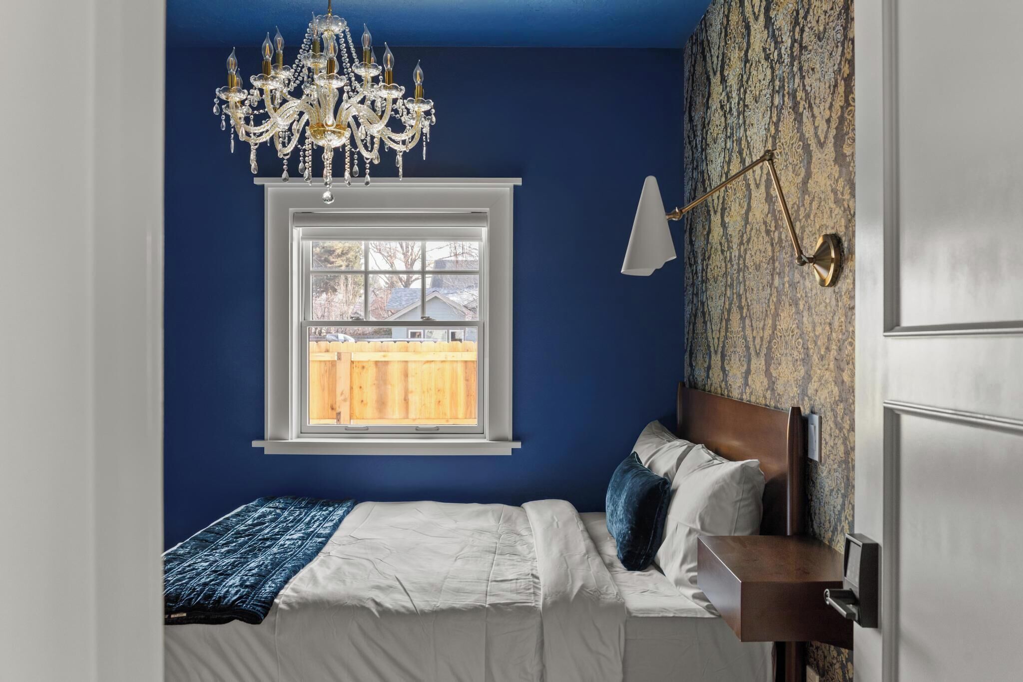 Un dormitorio con cama, candelabro, ventana y un papel tapiz decorado.