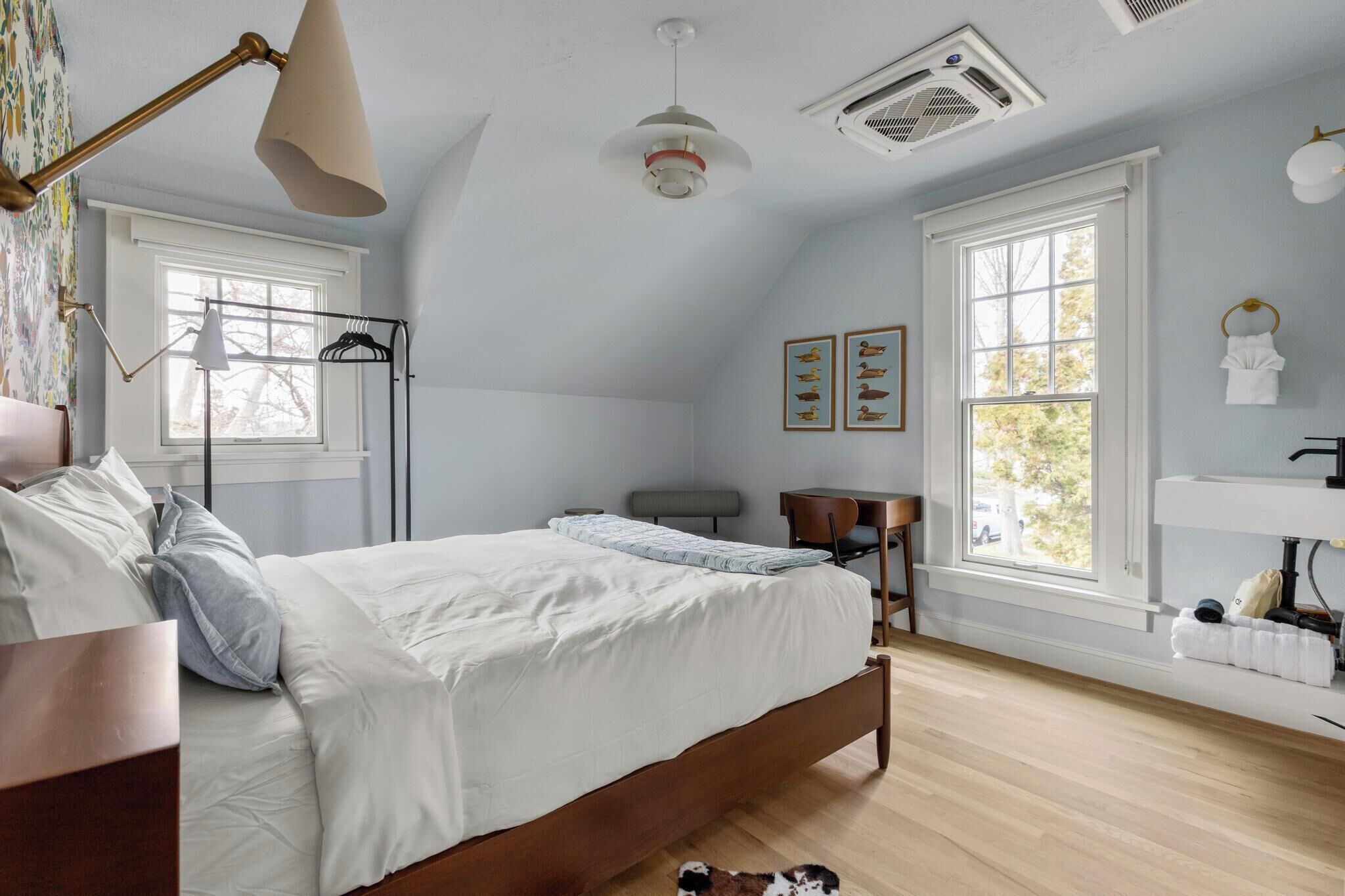 Un dormitorio con cama, escritorio, silla, perchero y ventana con vistas a árboles.