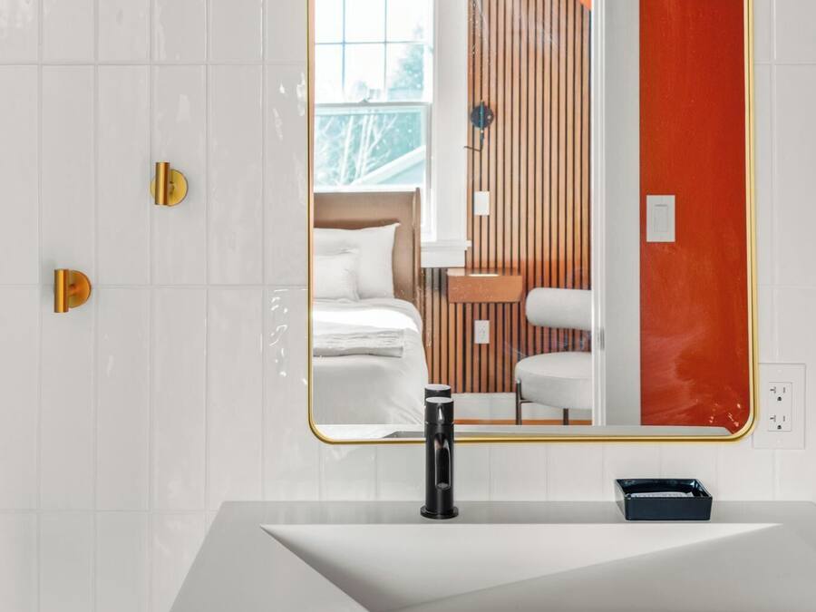 A modern bathroom with a white vanity, a large mirror, and a red accent wall.