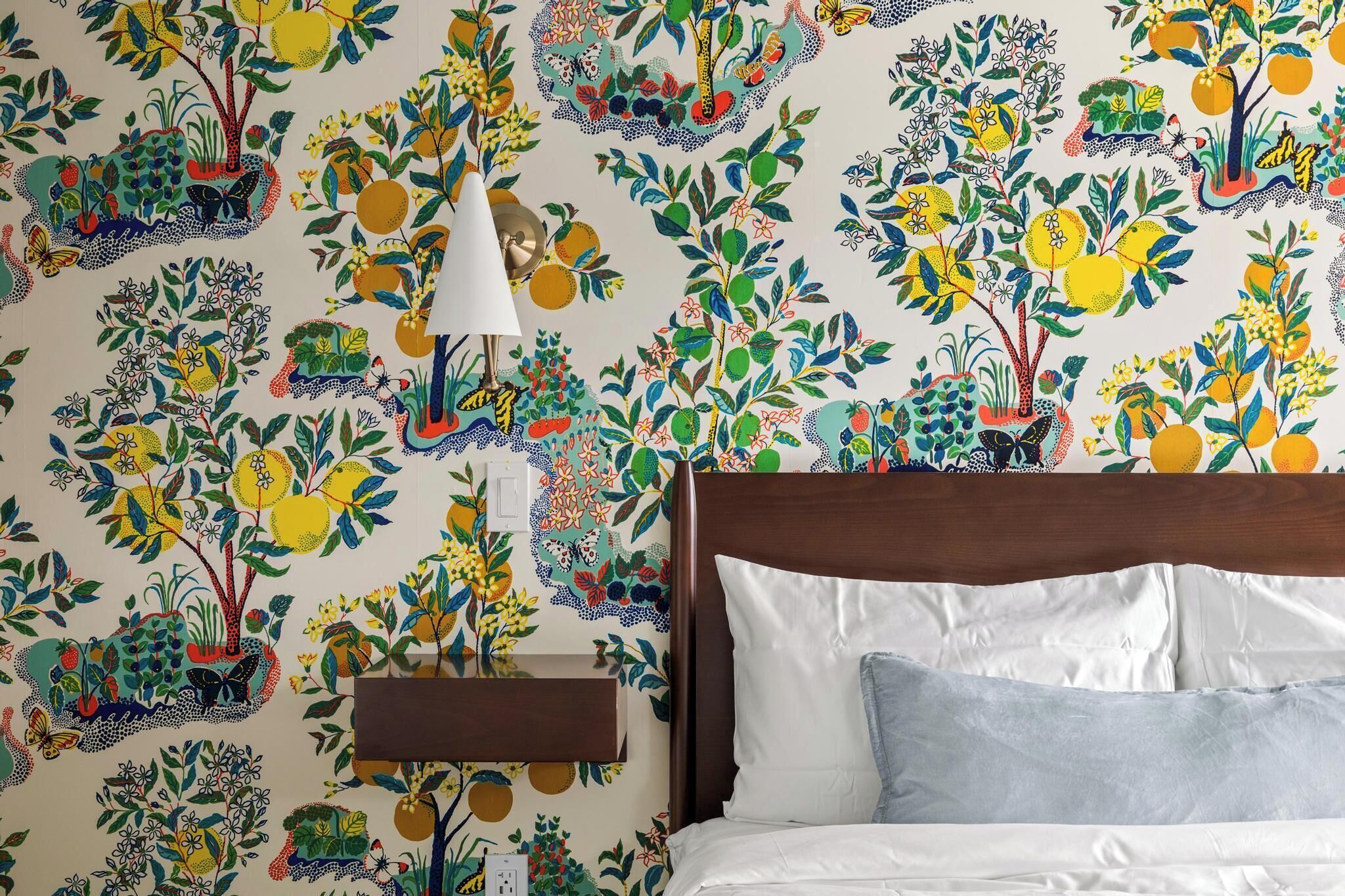 Un dormitorio con una cama, una mesita de noche y una pared con un estampado floral colorido.