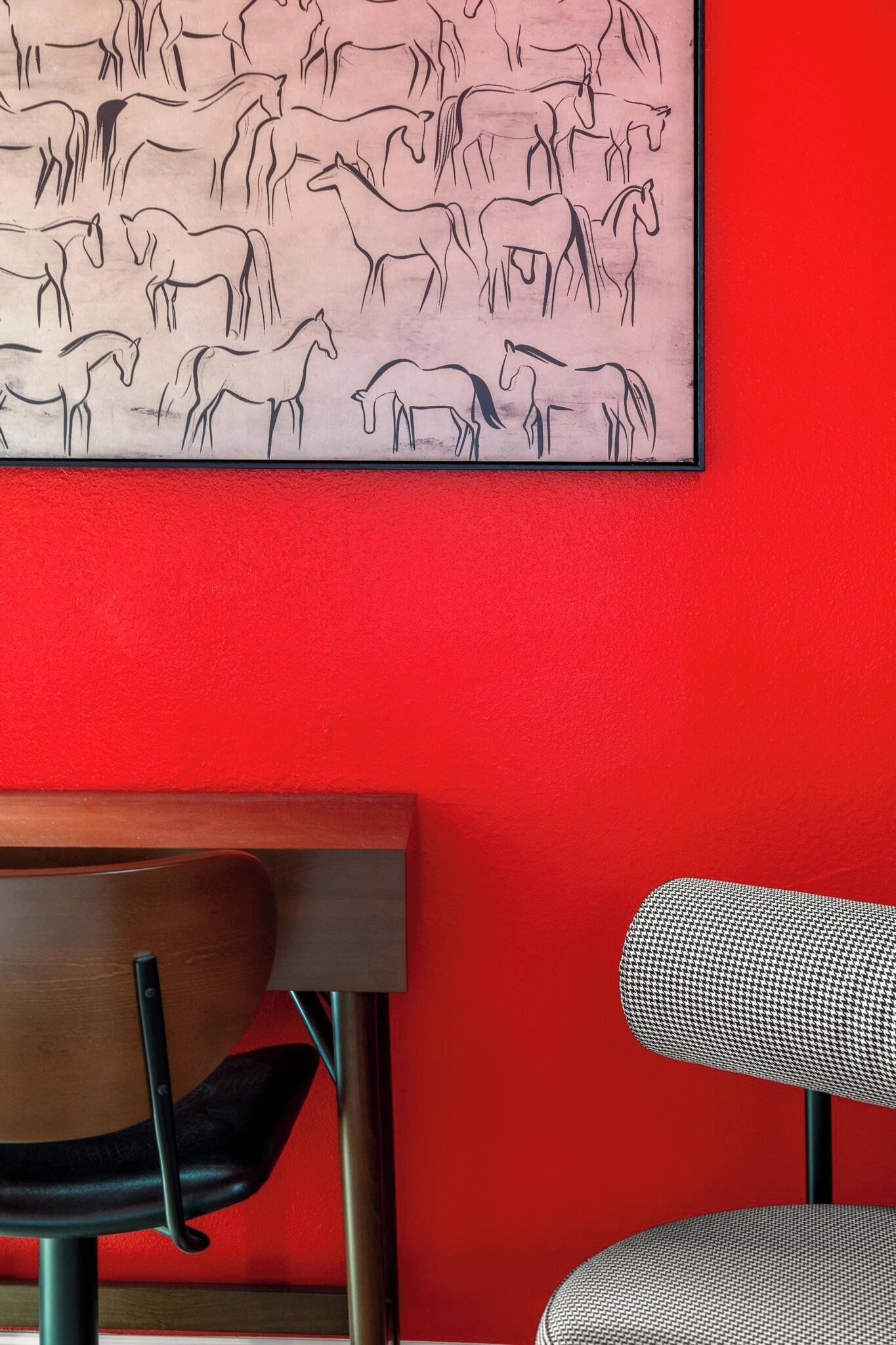 A framed black and white horse painting on a red wall, a wooden desk, and two chairs.
