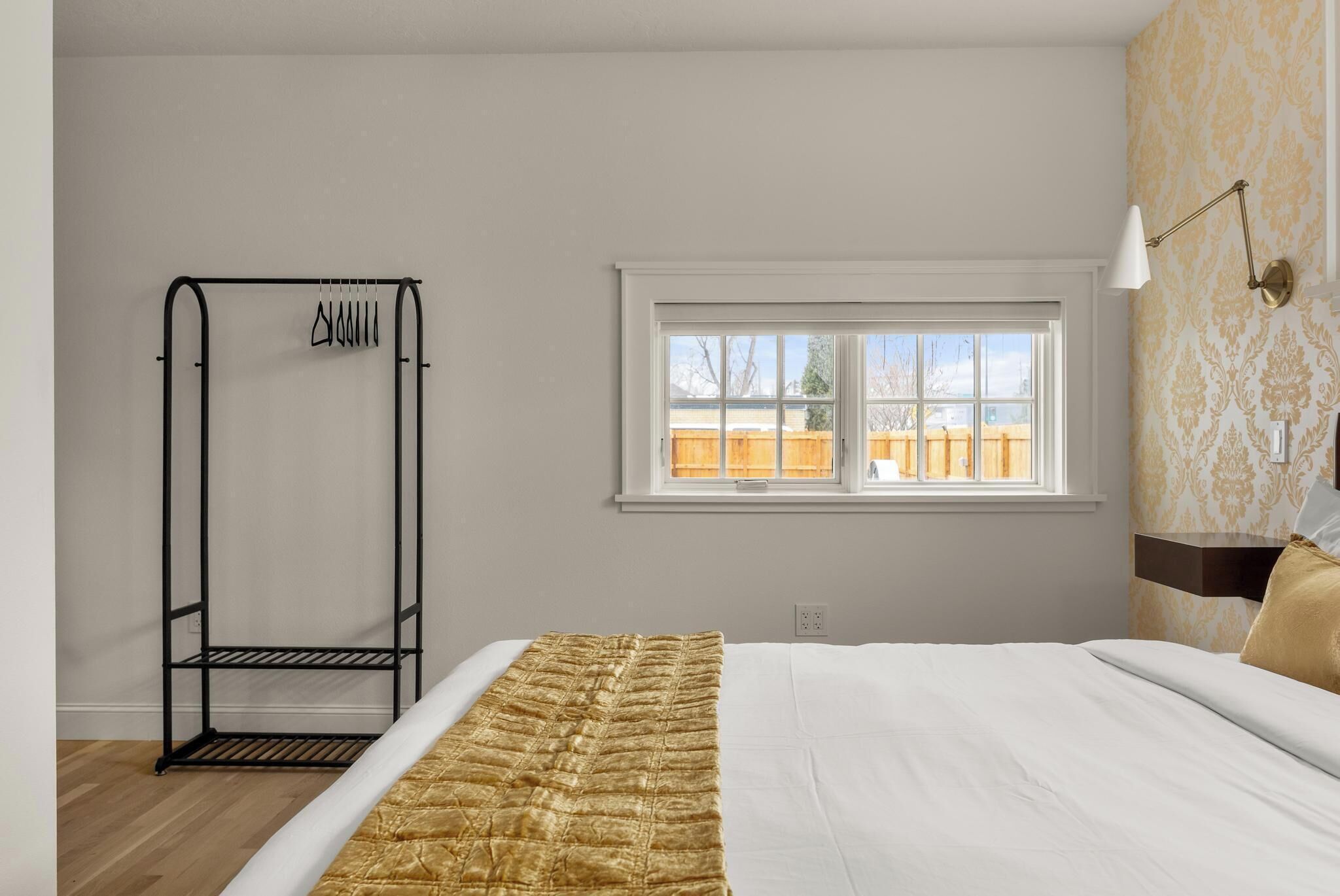 A bedroom with a bed, a window, a wall-mounted lamp, and a metal rack.