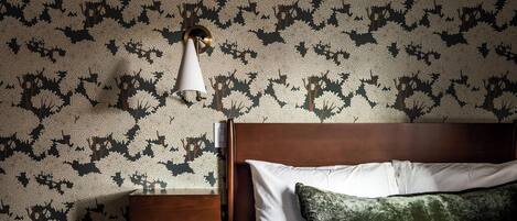 A bedroom with a bed, a nightstand, a lamp, and a wall with a tree pattern.