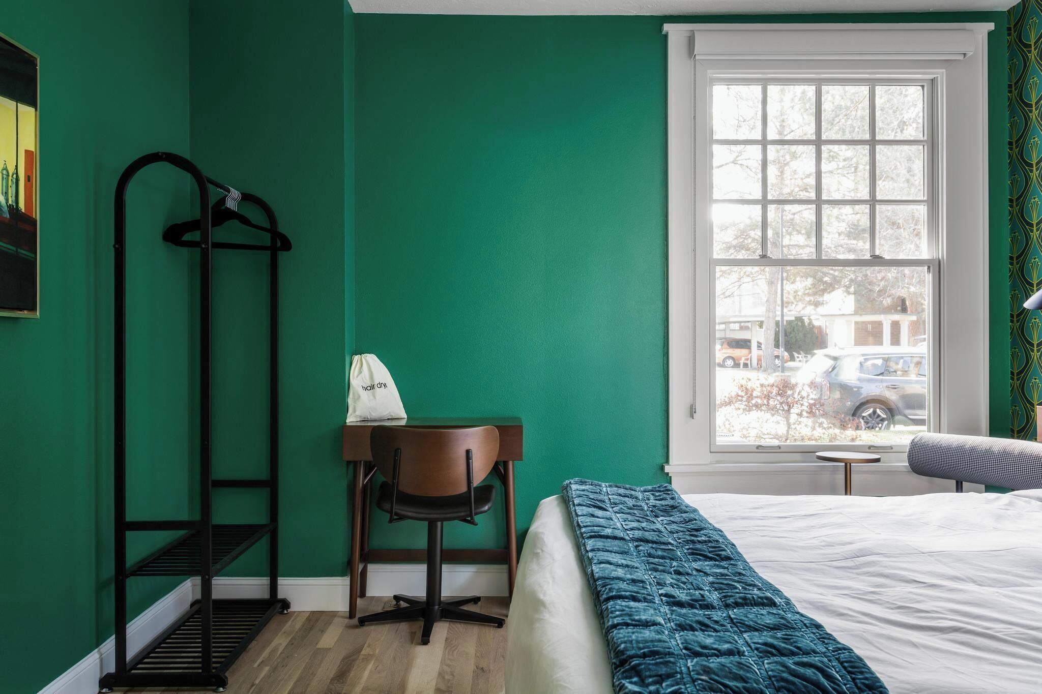 Una habitación con cama, un escritorio con silla, perchero y ventana con vista al exterior.