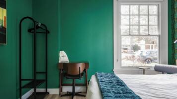 Una habitación con cama, un escritorio con silla, perchero y ventana con vista al exterior.