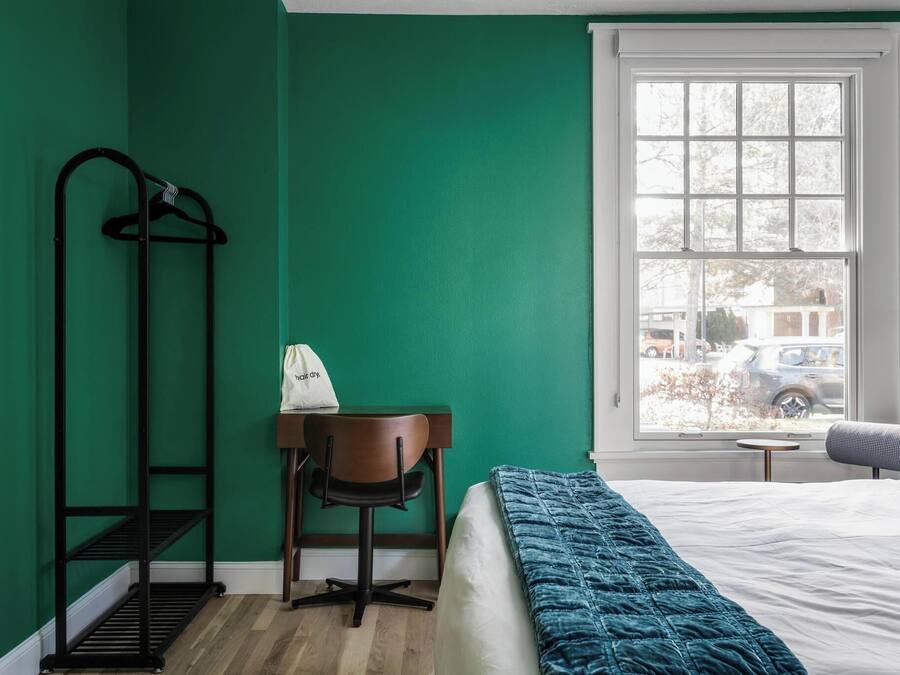 Una habitación con cama, un escritorio con silla, perchero y ventana con vista al exterior.