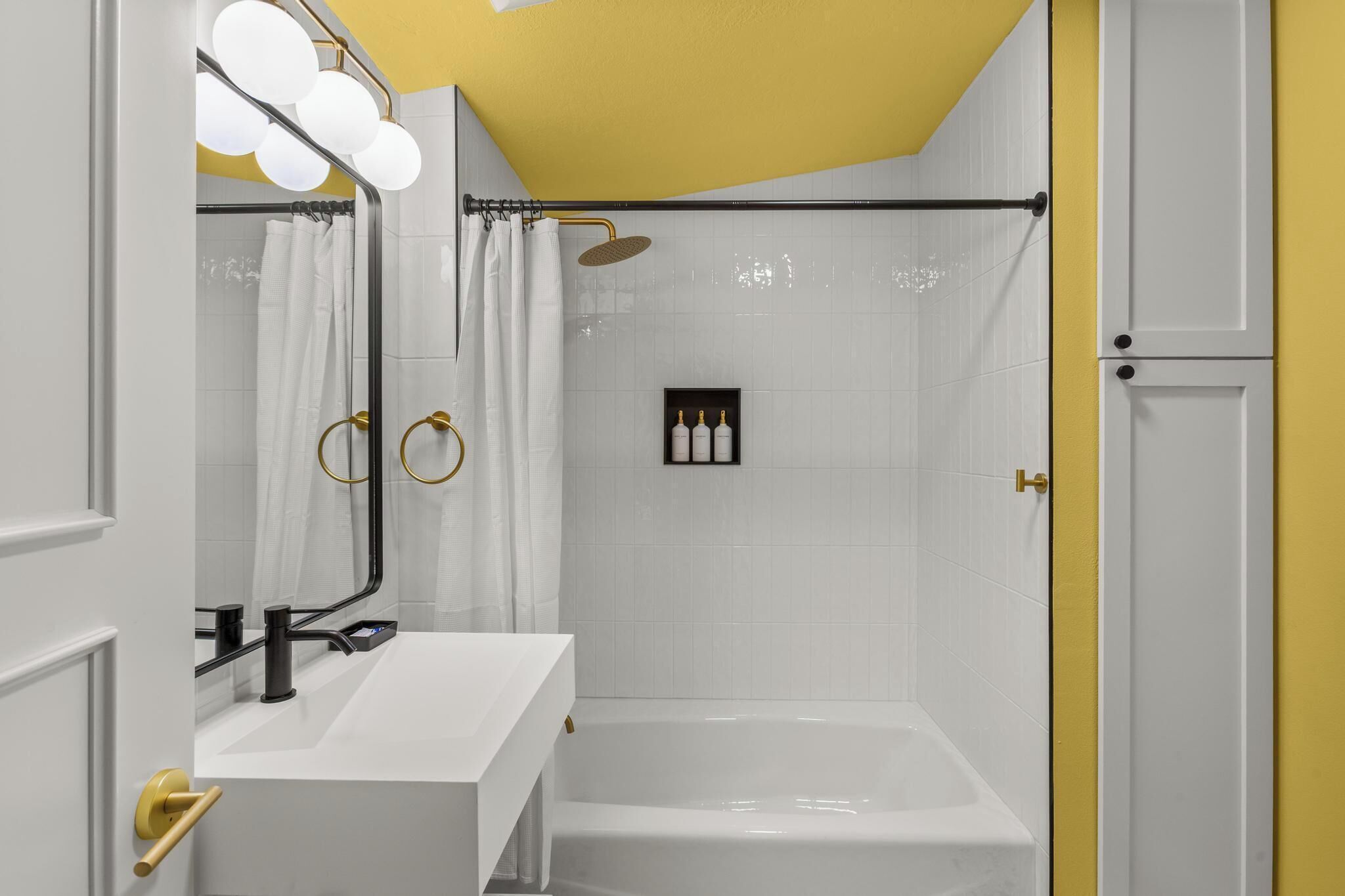 Un baño con bañera, lavamanos blanco, espejo con luces y cortina de ducha.