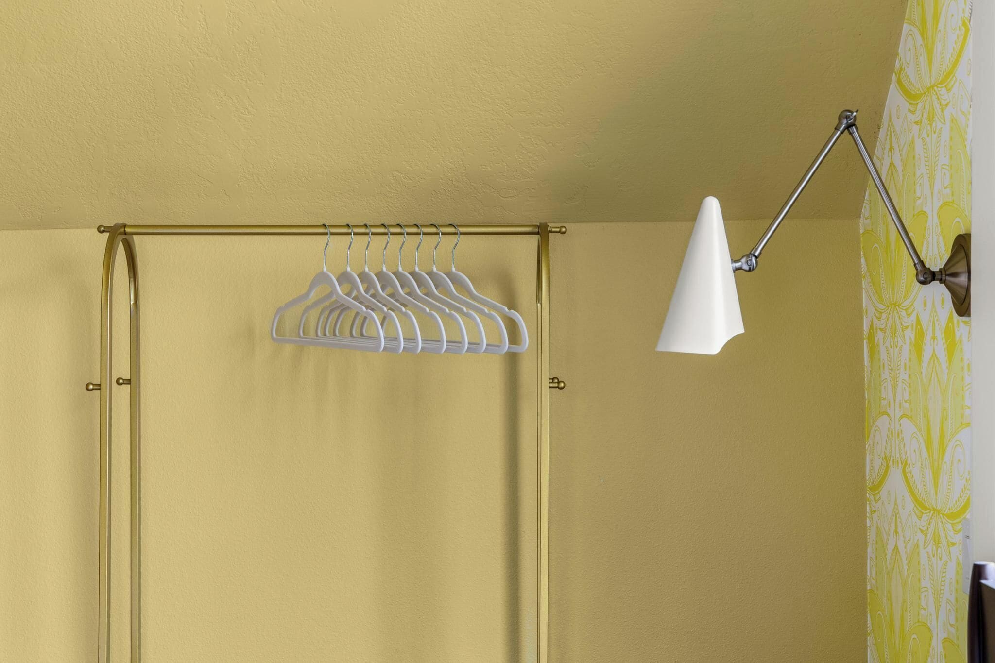 Een kamer met een gele wand, een witte hangende kledingrek en een witte vloerlamp.