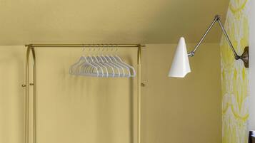 Een kamer met een gele wand, een witte hangende kledingrek en een witte vloerlamp.