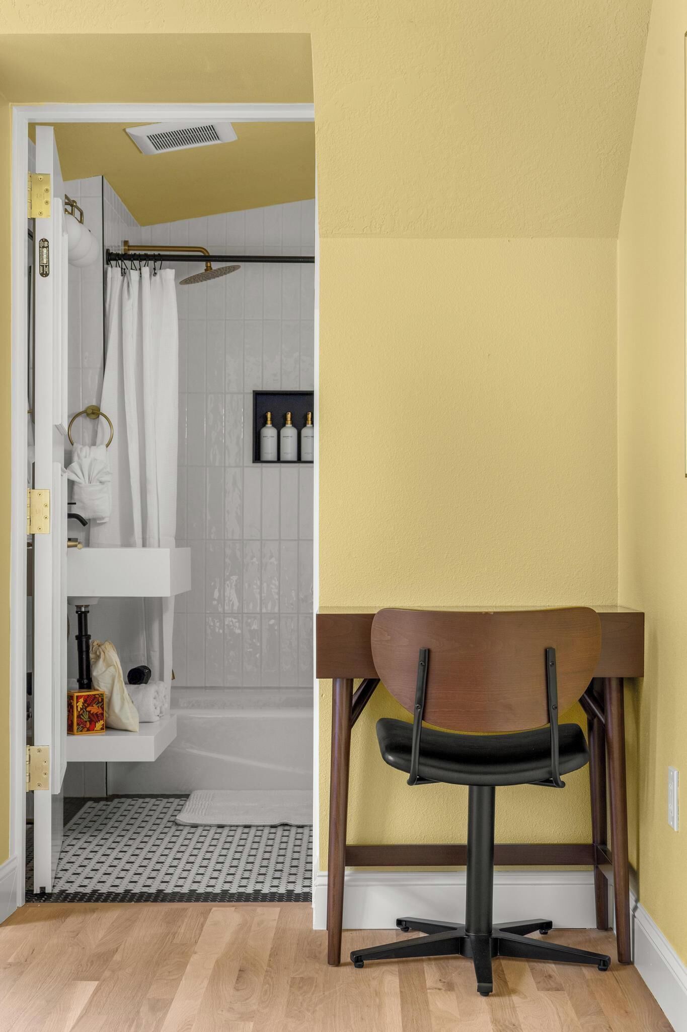 Un baño con ducha, inodoro y lavamanos. Hay una silla y una mesita en la esquina.