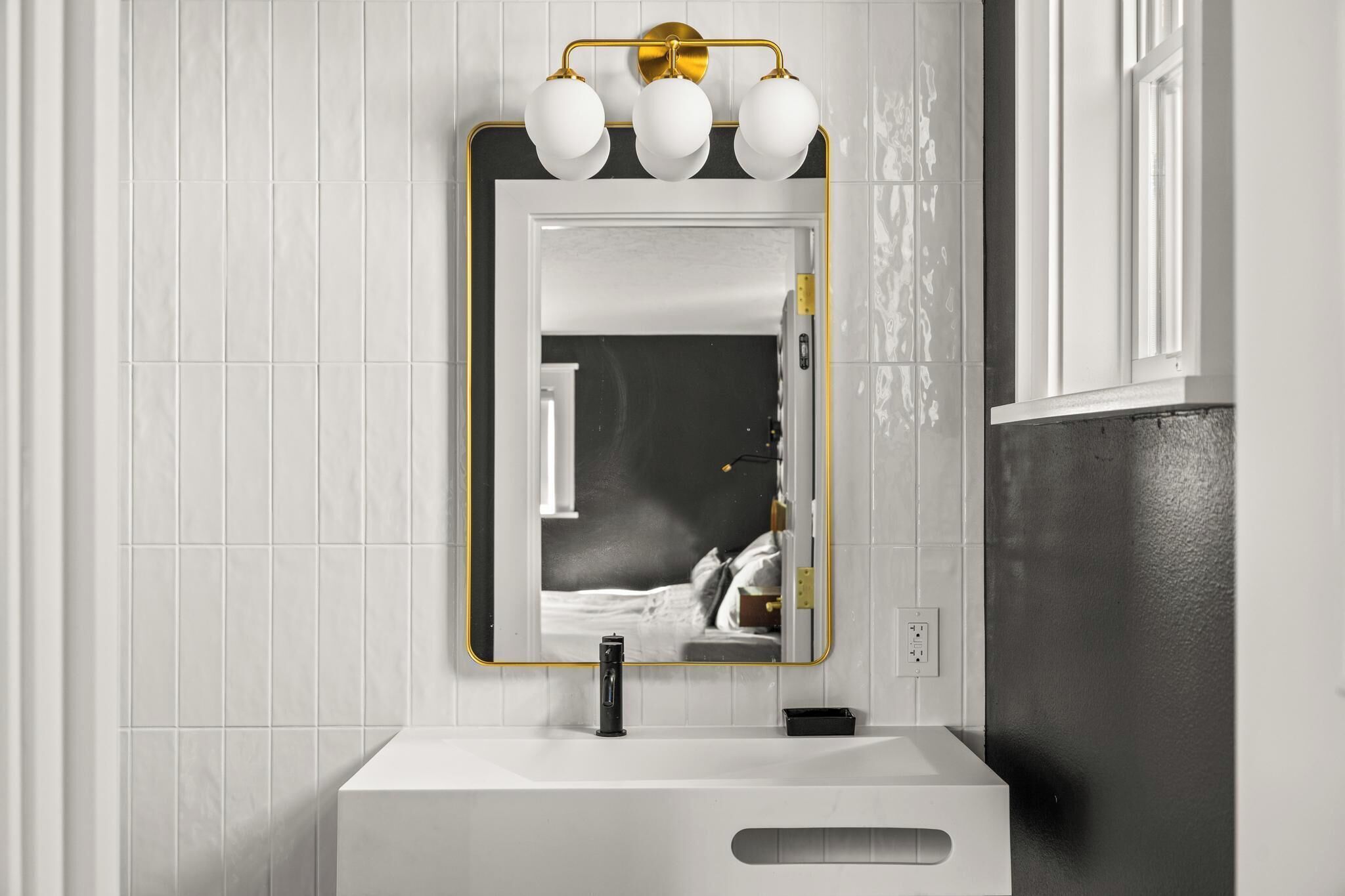 Een badkamer met een wit wastafel, een spiegel met gouden lijst, en een wandlamp.
