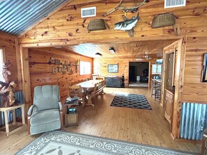A wooden cabin interior with a dining area, a fireplace, and a kitchen visible through an open doorway.