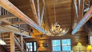 Een rustiek houten interieur met een wenteltrap, een kroonluchter met gewei decoraties en een gezellige zithoek.