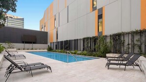 Un edificio moderno con piscina, sillas de descanso y un patio empinado.