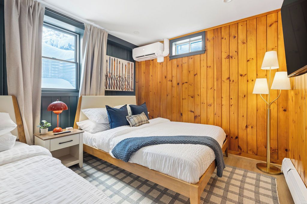 A bedroom with a wooden wall panel, a bed with white bedding, a nightstand with a lamp, and a window with curtains.
