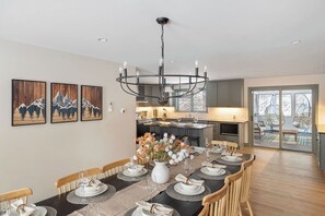 A dining area with a long table set for six, a chandelier, and a kitchen in the background. - Sleeps 18+| Hot Tub| Sauna | 7BR Mountain Retreat (Conway)