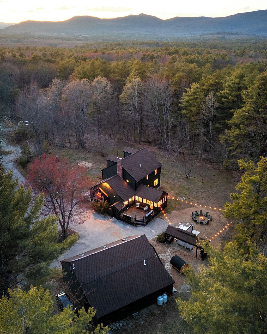 A large, multi-story cabin with a deck and outdoor seating area, surrounded by a forested landscape.
