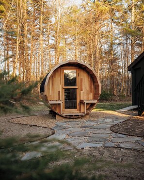 A wooden cabin with a circular design, a door, and a window, surrounded by a stone pathway and forest. - Sleeps 18+| Hot Tub| Sauna | 7BR Mountain Retreat (Conway)