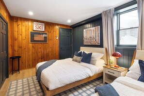 Et hotelværelse med trævæg, en seng med mange puder, et natbord med en lampe og et vindue med gardiner.