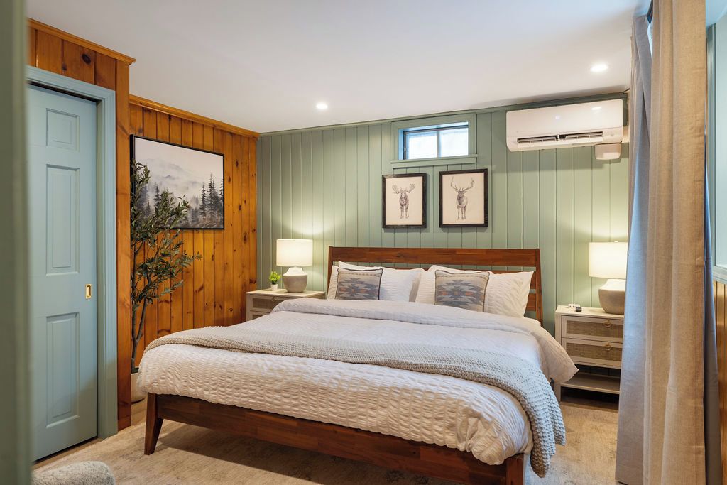Un dormitorio con una cama de madera, una mesita de noche, un aire acondicionado instalado en la pared y una puerta.
