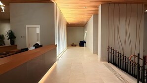 Et moderne receptionsområde med en træreception, en hvid væg med lodrette linjer og et flisegulv.