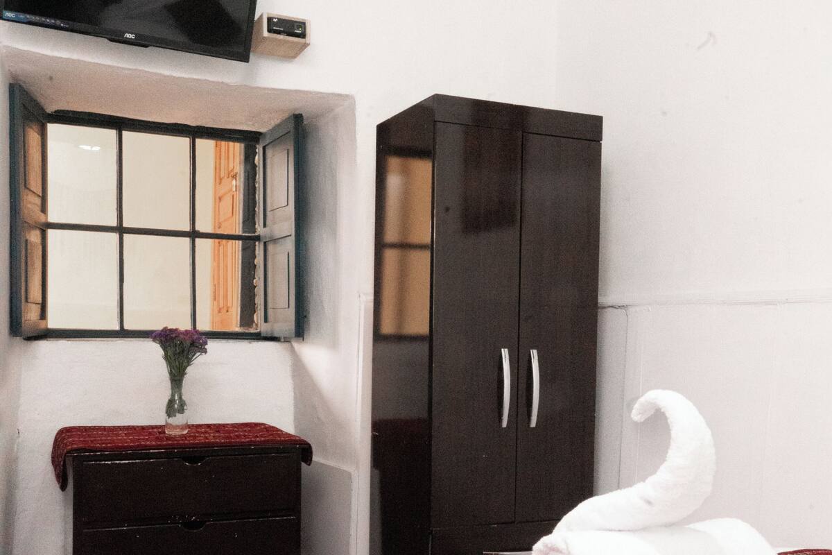 Habitación de hotel con cama, cómoda, televisor montado en la pared y armario.