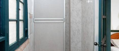 A bathroom with a shower, a door, and a window with a decorative frame.