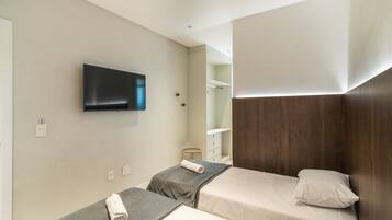 Habitación de hotel con dos camas, un televisor montado en la pared y un cabecero de madera.