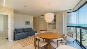 A modern living room with a round wooden table, a sofa, and a dining area with chairs. - Fully Equipped Stays Just Steps From the sea in Pereque Mtrs (Porto Belo)