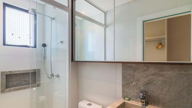 Une salle de bain moderne dotée d’une douche à parois de verre, d’un comptoir en marbre et d’un grand miroir.
