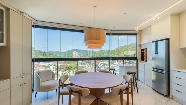 A modern kitchen with a large island, stainless steel appliances, and a view of a cityscape through large windows. - Fully Equipped Stays Just Steps From the sea in Pereque Mtrs (Porto Belo)