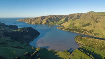 An aerial view of a coastal landscape with a large body of water, green hills, and a small settlement.