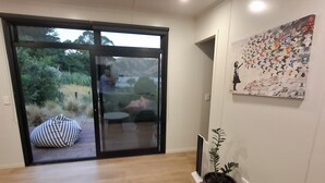 An interior space with a sliding glass door leading to a garden, a potted plant, and a wall-mounted artwork. - Overleigh Eco-Pod (Port Levy)