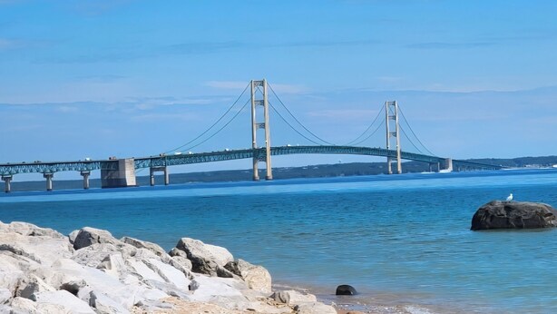 A large suspension bridge over a body of water with rocky shoreline in the foreground.