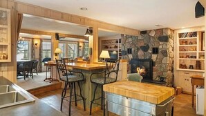 A cozy kitchen with a stone wall, wooden bar stools, and a fireplace.