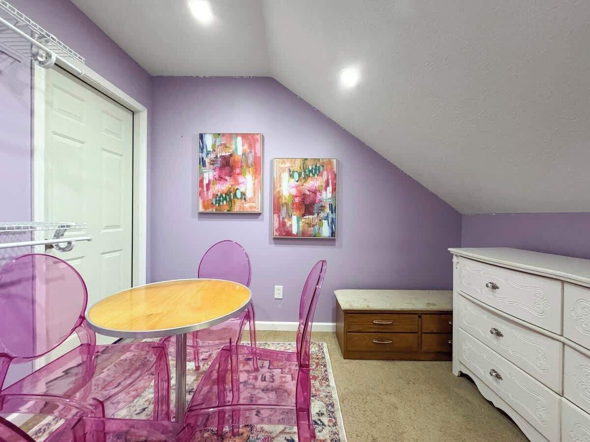 A room with a purple wall, a white dresser, a wooden bench, a table with chairs, and two paintings.