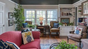 Ein Wohnzimmer mit einem roten Sofa, Sesseln, einem Couchtisch, einem Bücherregal und einem großen Fenster.