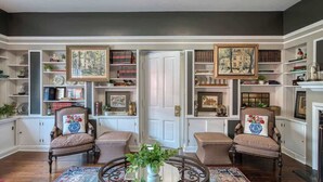 Una habitación con dos sillones, una mesa redonda y una estantería llena de libros y objetos decorativos.