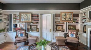 A room with two armchairs, a round table, and a bookshelf filled with books and decorative items. - Large Historic Mansion Near Cleveland | Sleeps 12 (Berea)