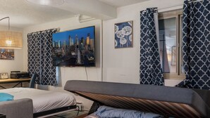 Ett modernt sovrum med en tv-skärm som visar en stadsbild, mönstrade gardiner och en säng med en sänggavel.