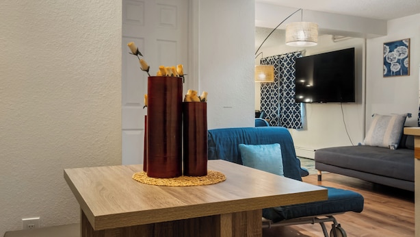 Ett modernt vardagsrum med ett matbord i trä, två barstolar, en blå soffa och en grå divansoffa.