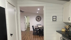 A kitchen with white cabinetry, a wooden dining table with chairs, a clock on the wall, and a stove.