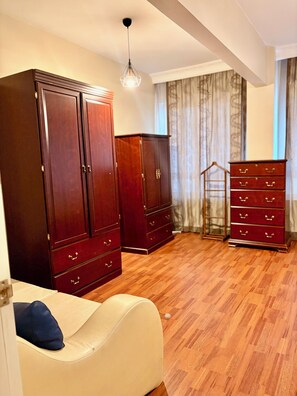 Ein Zimmer mit Holzboden, einem großen Kleiderschrank, einer kleineren Kommode und einem Sofa mit Kissen.