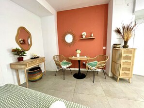 A room with a bed, a desk with a mirror, two wicker chairs, a round table with a vase, a cabinet, and a potted plant. - Stylish Studio by M. Zambrano Train St, 15' walk to beach & city center (Málaga)