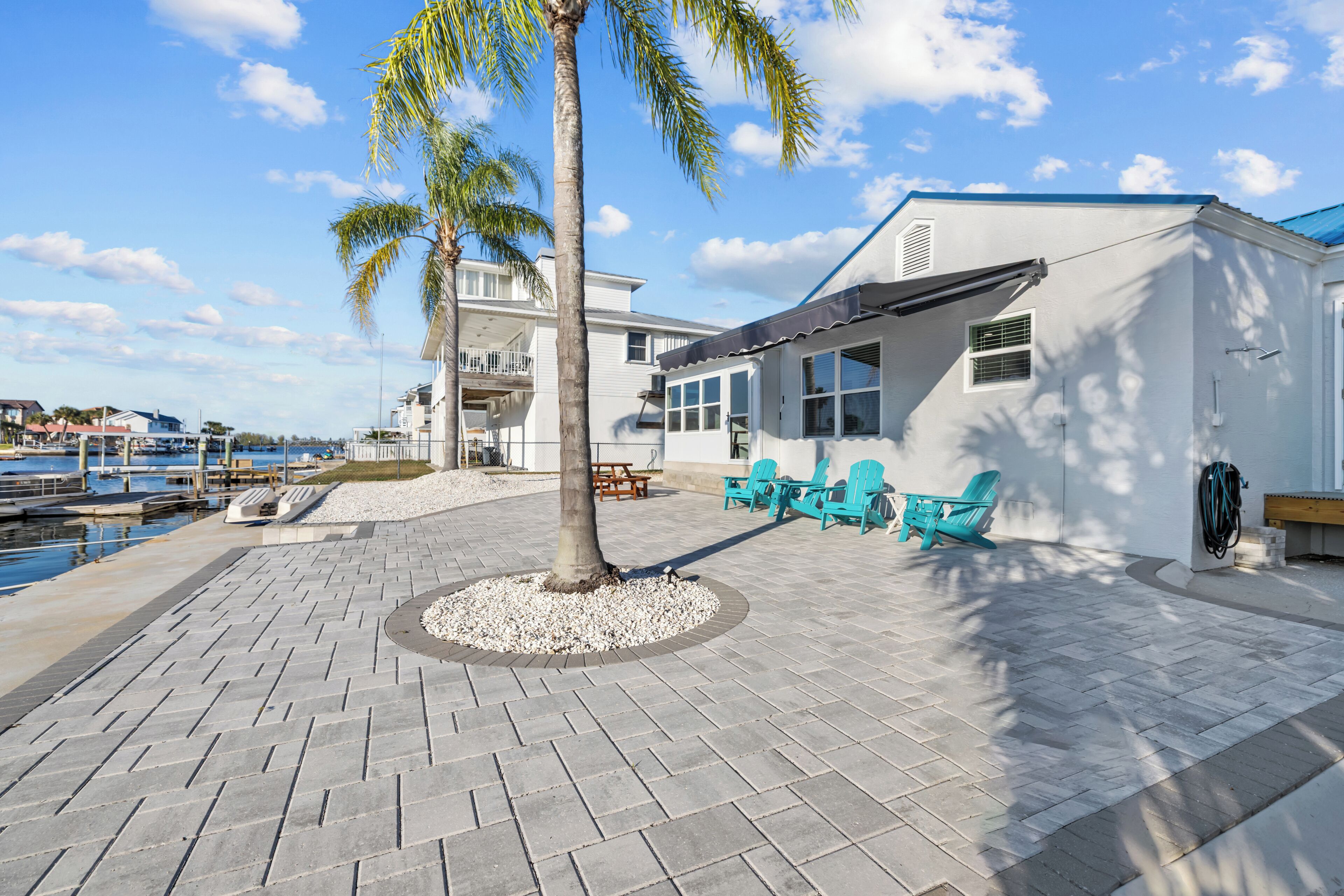 A beachfront property with a patio area featuring a palm tree, blue chairs, and a view of the marina.