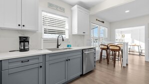 A modern kitchen with grey cabinets, a coffee maker, and a sink. There are three wooden bar stools and a window with blinds. - Newly remodeled 3-bedroom waterfront home in amazing Hernando Beach (Hernando Beach)